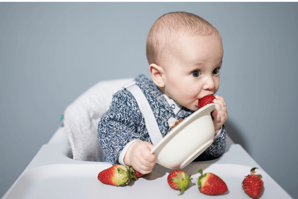 Baby weaning with strawberries, starting solids, child in high chair exploring new foods.